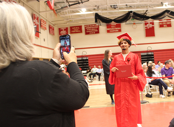 An adult takes a picture of a student holding the diploma