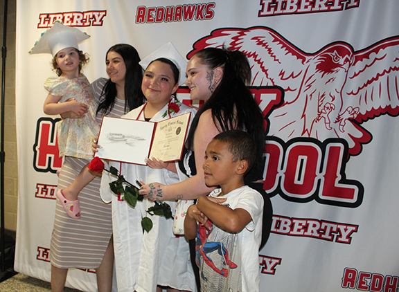A family poses for a photo with a young girl wearing a graduation cap in front of a LHS background