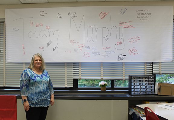 A woman stands next to a sign that reads Team Murphy and has messages of support
