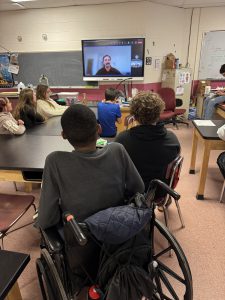 Students seated at a table take part in a video conference.