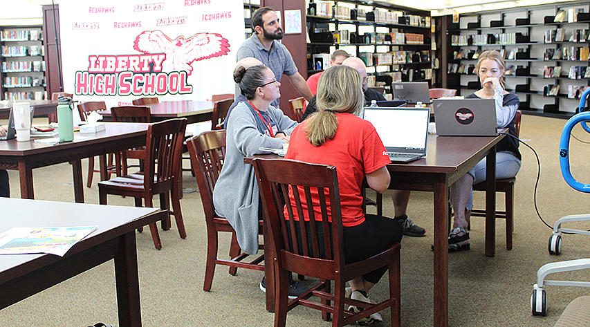 People gather around a table with computers in a library.