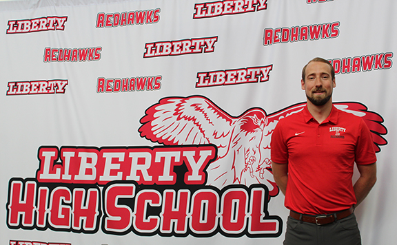 A man poses in front of a Liberty High School backdrop