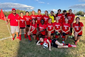 A girls soccer team poses for a photo on the edge of a soccer field.