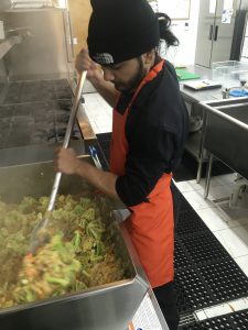 A cook stirs vegetables in a large cooking pot