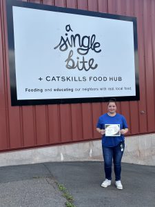 A student holds a certificate in front of a sing for a Single Bite