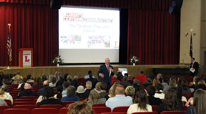 A man in front of a screen with "Our Strategic Plan and intents" on a screen.