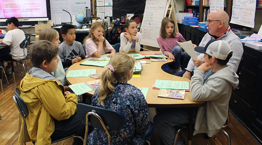 A teacher leads a lesson to a group of students seated around a semicircular table