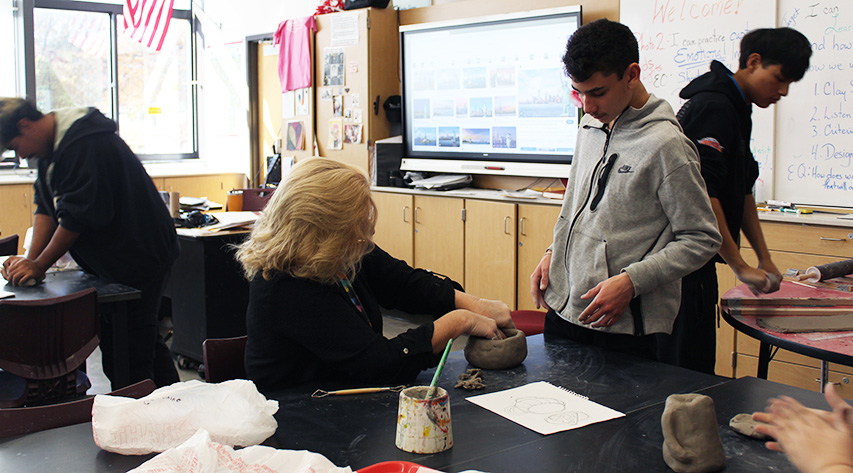 A teacher demonstrates how to shape a clay bowl to a student