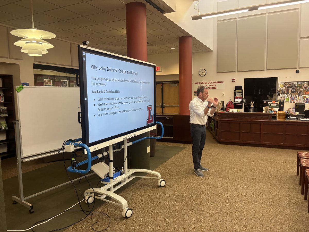 A man speaks in front of a large screen