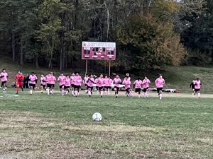 The boys soccer team, dressed in pink shirts for the annual pink out game, run to the center of the field.