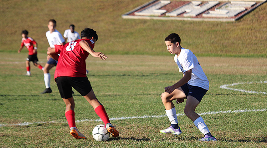 A Liberty soccer player in red keeps the ball away from an opponent in white