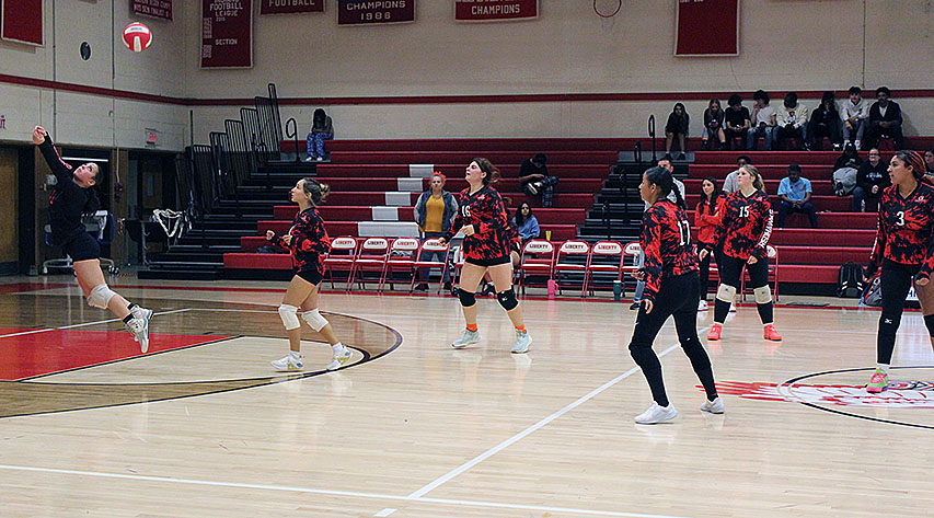 A volleyball player keeps the ball in play as her teammates watch the ball.