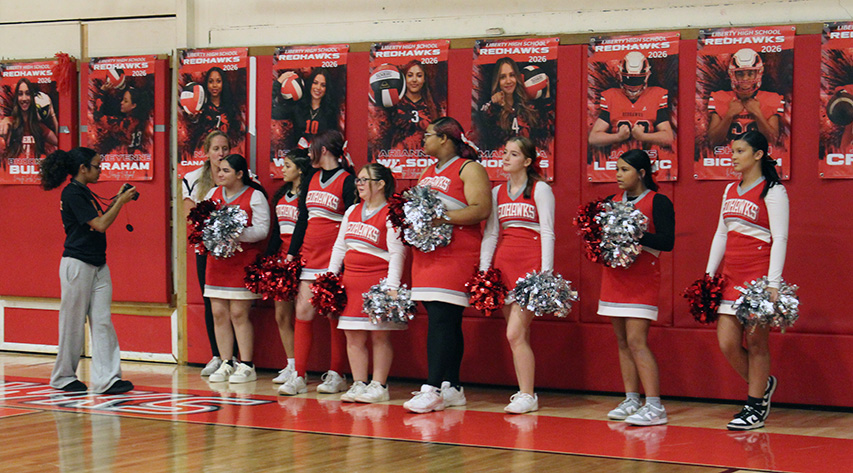 A student takes pictures of cheerleaders lined up against a wall with photos in the background