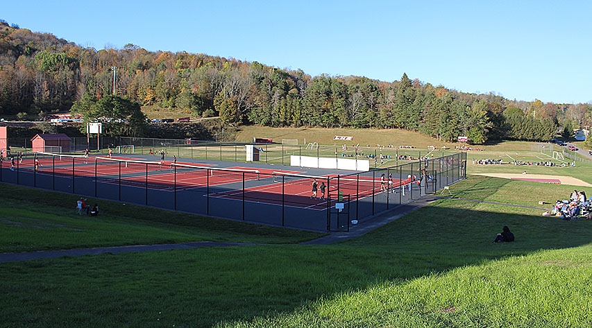 Tennis matches take place in an upper level as a soccer game takes place in the lower field