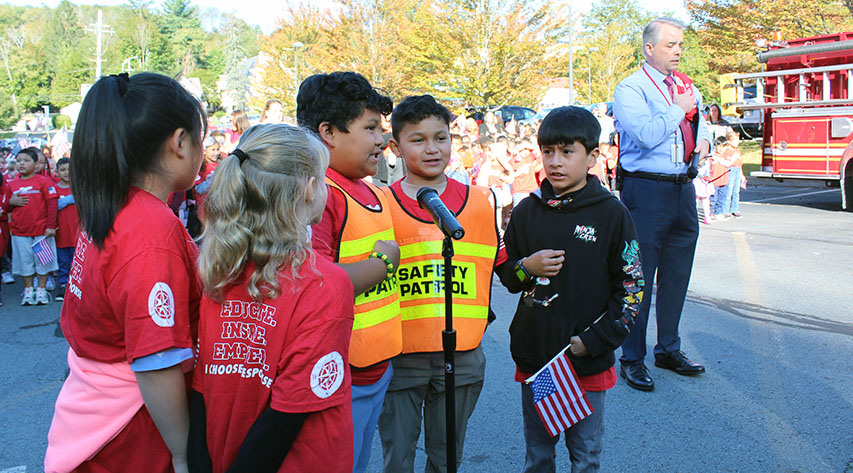 five students say the pledge as an adult stands behind them