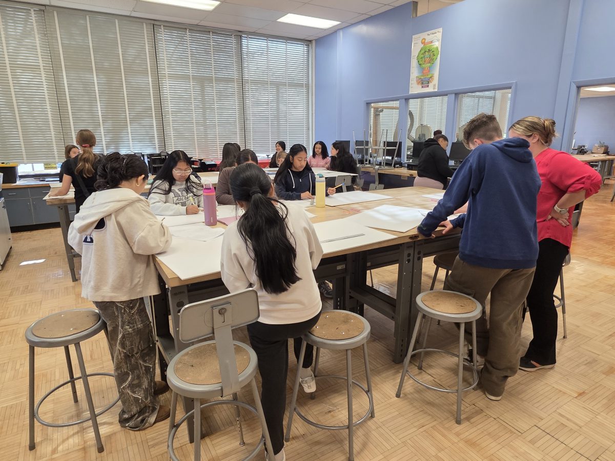 Students work on plans for greenhouses at a large table.