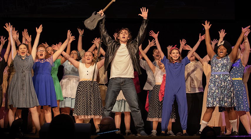 Students raise their hands and sing during a performance on stage