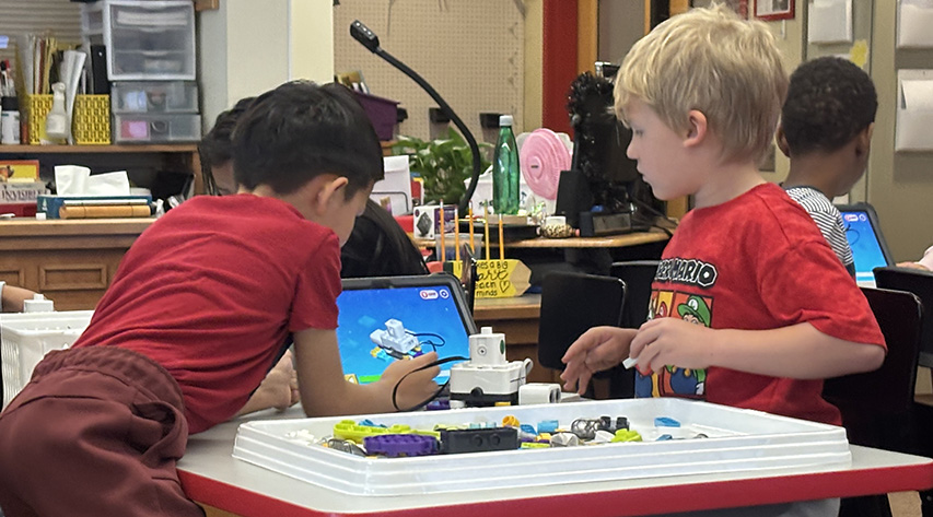 Two students look at a screen as they build a robot.