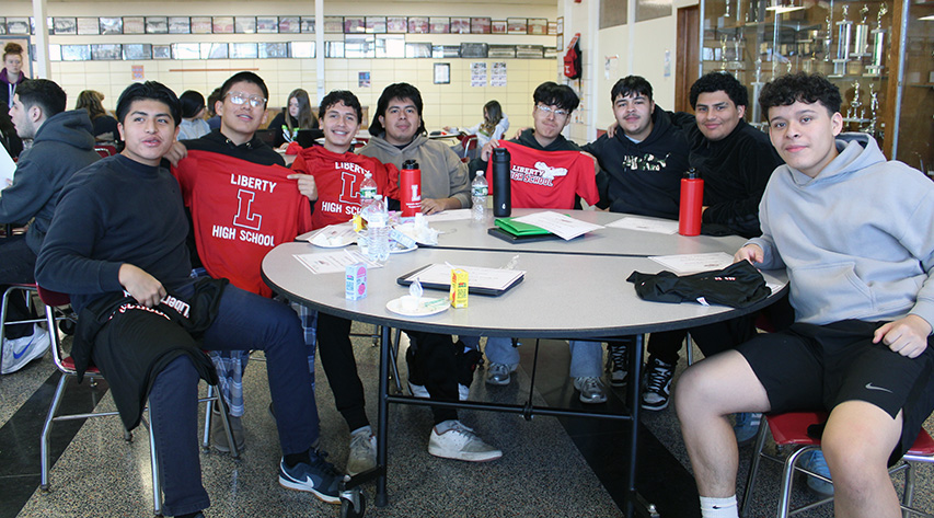 Students pose around a table with Liberty Redhawk T-shirts and bottles.