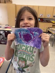 A student displays a painting of heart.