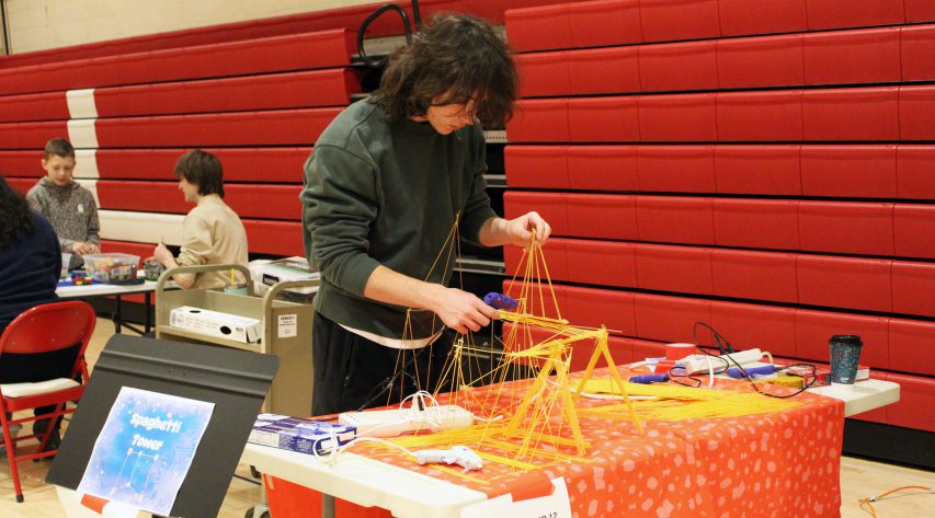 A student uses a glue gun to build a spaghetti tower