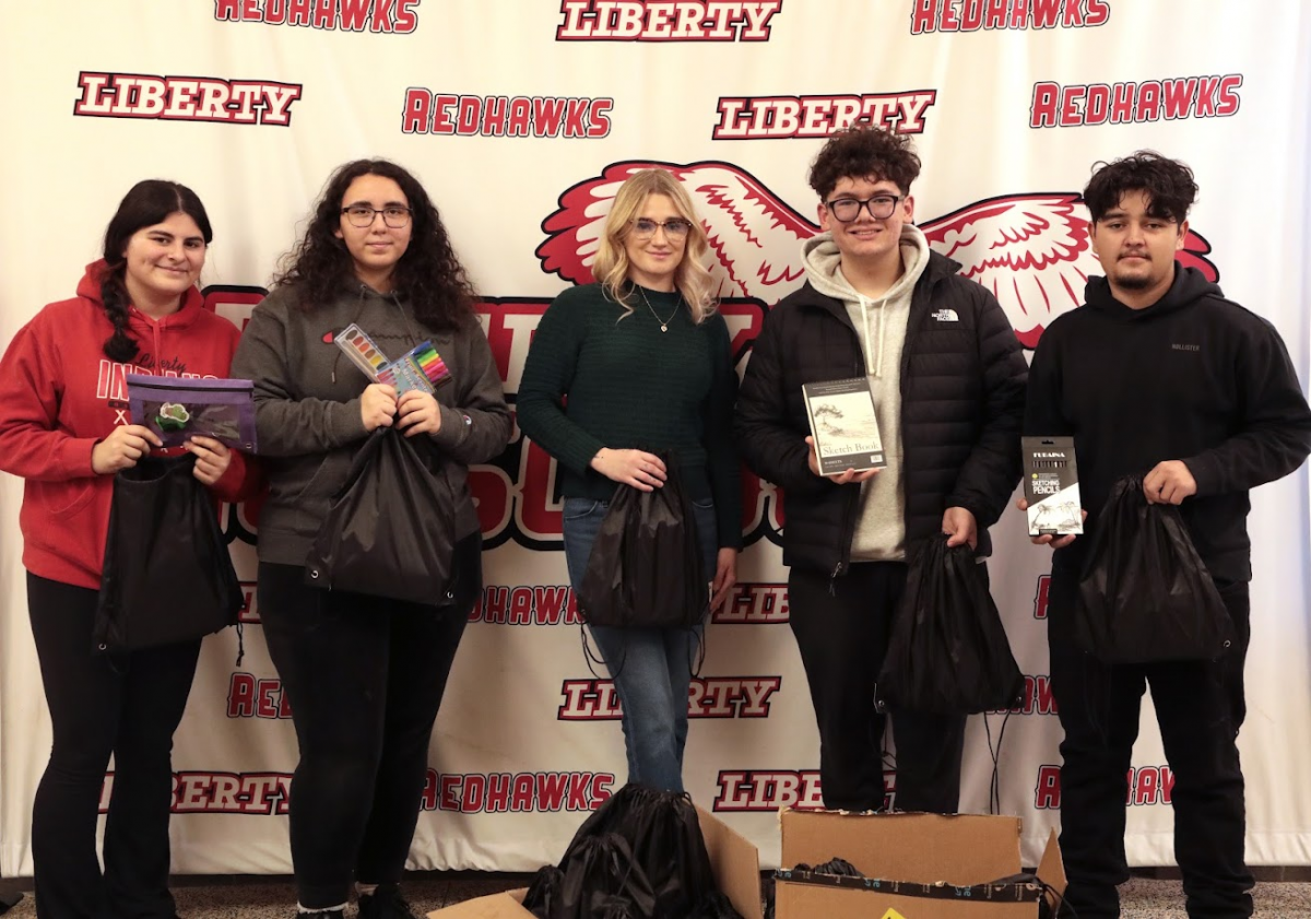 five people hold art supplies standing in front of a Liberty Redhawks banner.