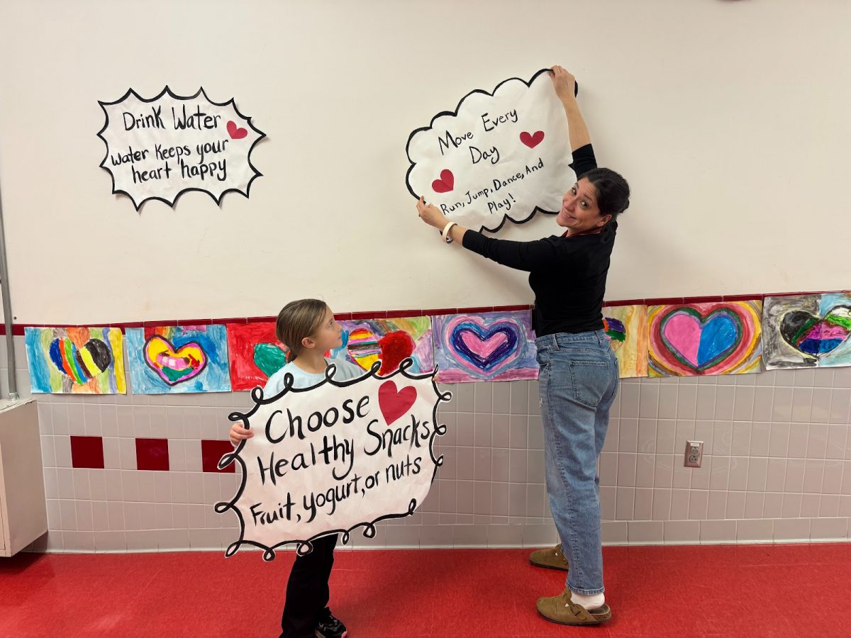 A teacher hangs up a sign promoting healthy snacks as a student holds one near.