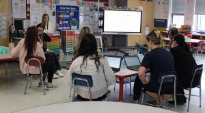 Teachers review lesson plans  seated at tables with computers in front of them.
