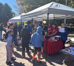 Students and others gather around a table at a tent