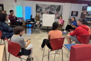 Students and others sit in chairs in a circle.