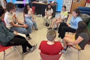 Students and others sit in chairs in a circle.