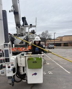 A student holds a pole while in the bucket of a bucket truck positioned near the ground