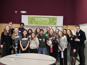 Members of the FFA chapter pose for a photo in front of a size that reads discovery kitchen