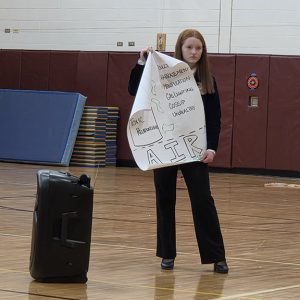 A student holds a large piece of paper with Air written on it.