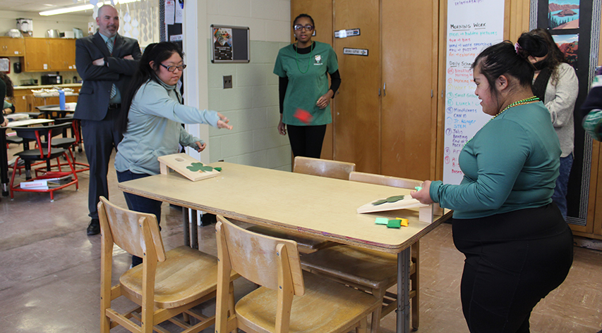 Two students play table cornhole as a student and two adults watch