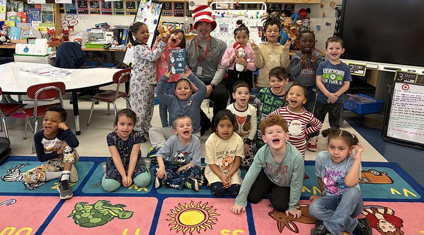 A man in a Cat in the Hat red and white striped hat poses with a group of students.
