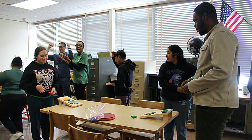 People cheer in the background as two people play table cornhole