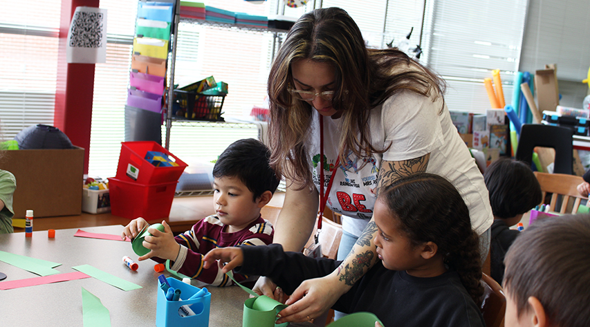 An adult helps students make green paper chains