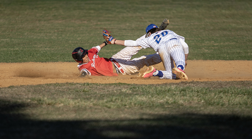 A lLberty student slides as an opposing player tries to tag him on the baseball diamond.