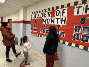 A family looks at Leader of the month bulletin board