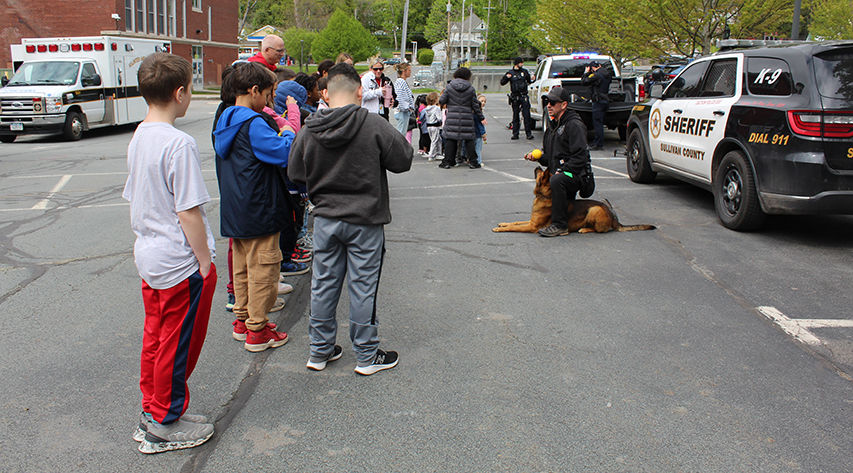A police officer work with his K-9 partner as students watch