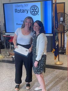 Two people pose for a photo in front of a screen that reads Liberty Rotary