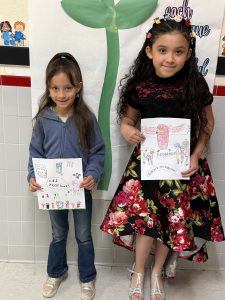 Two students hold up the artwork that will be on the cover and back cover of the LES yearbook
