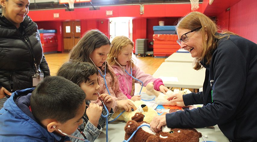 A woman speaks to children as they listen to teddy bears' "hearts" with stethoscopes