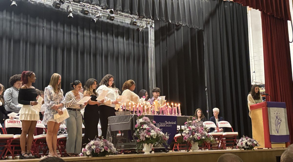 Students stand on a stage holding candles and papers during an induction ceremony.
