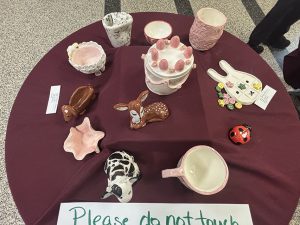 A variety of painted ceramic sculptures sit on a round table with a sign that says please don't touch.