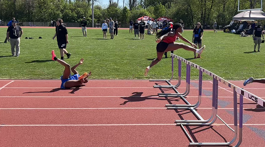 An athlete clears a hurdle as another athlete falls behind her.