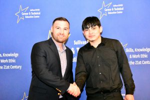 Two men shake hands in front of a blue backdrop with "Sullivan BOCES Career & Technical Education Center" text.