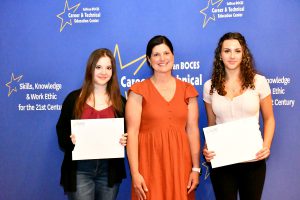 Three smiling individuals stand in front of a blue backdrop with "Sullivan BOCES Career & Technical Education Center" text and stars.