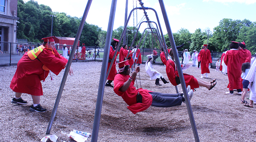 Seniors in caps and gowns swing on a swingset on a playground